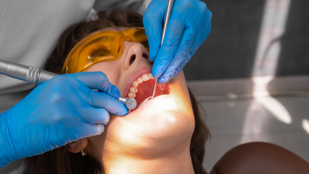 A lady in a dentist's chair with a dentist looking at her teeth.