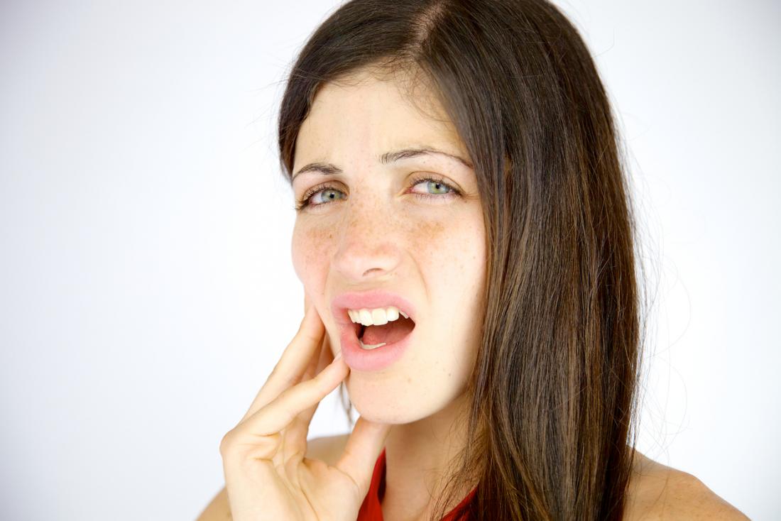 A lady with brunette hair, holding onto the outside of her mouth in pain.