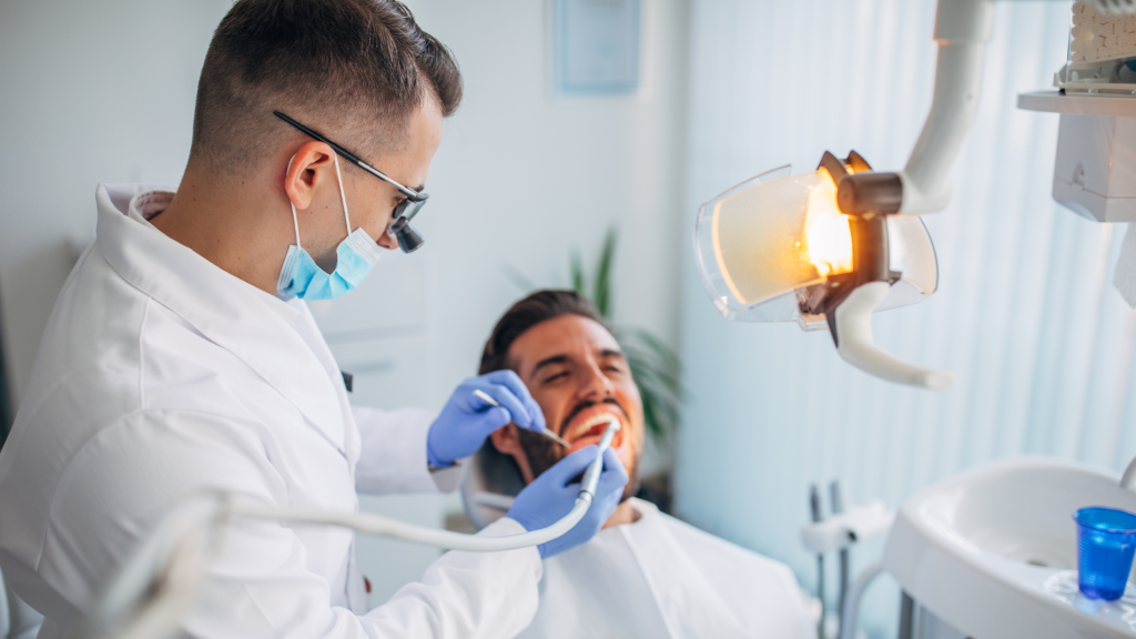 A dental patient in a the chair at a dental practice with a hygienist cleaning his teeth.